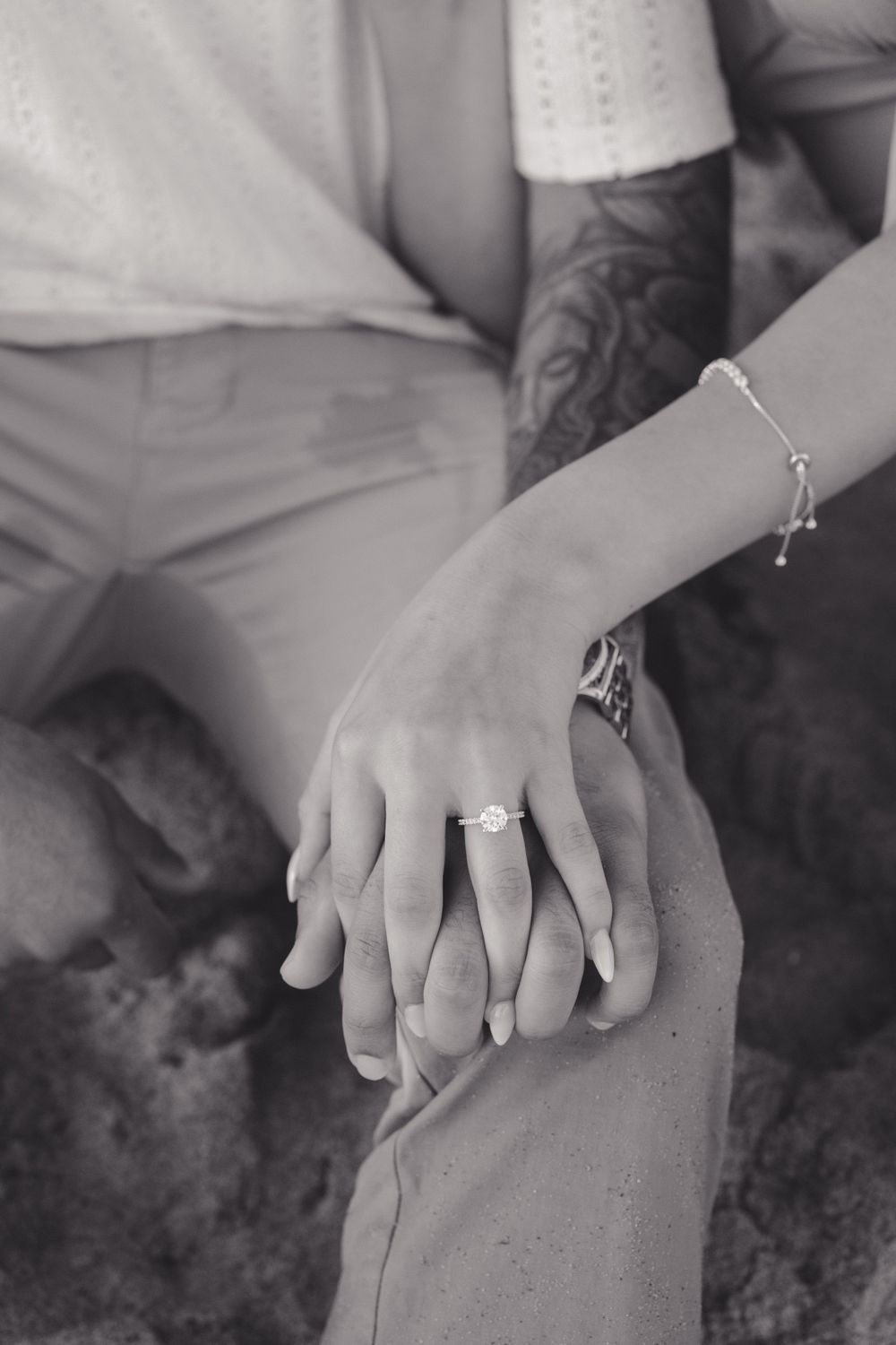 Close-up black and white photo of hands with engagement ring and tattoo showing romantic connection.