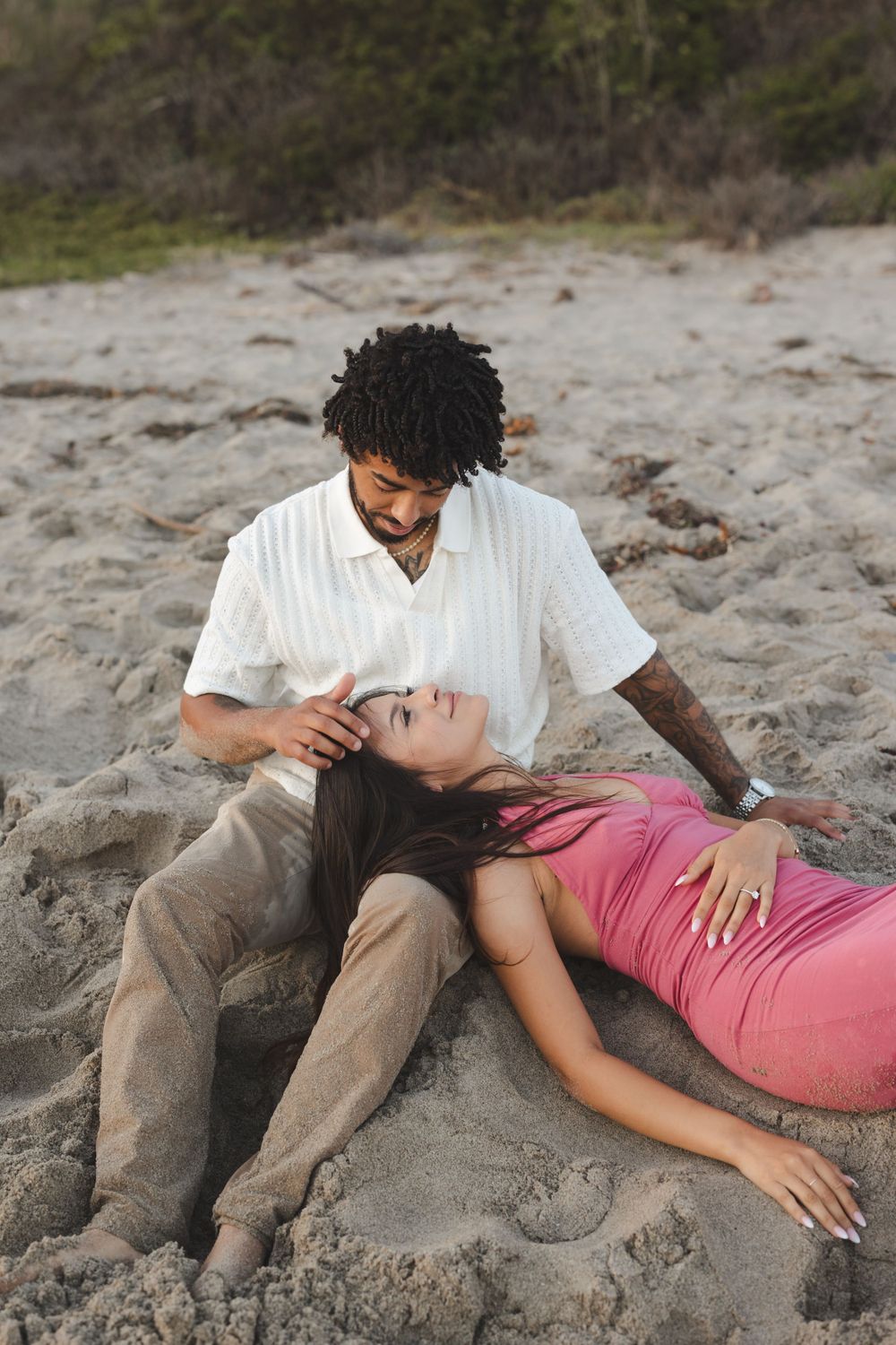 A couple shares an intimate moment while sitting on sandy beach during a romantic photoshoot.
