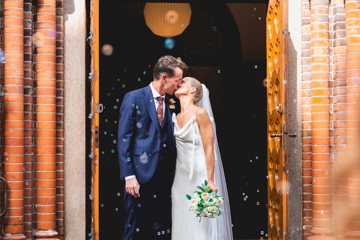 Newlyweds share an intimate moment under falling confetti in a church doorway.