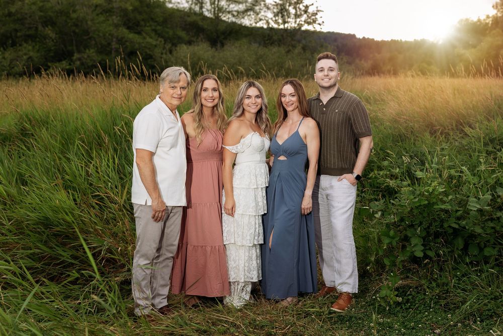 Family of five posing outdoors in a golden field at sunset, wearing coordinated earth-tone outfits.