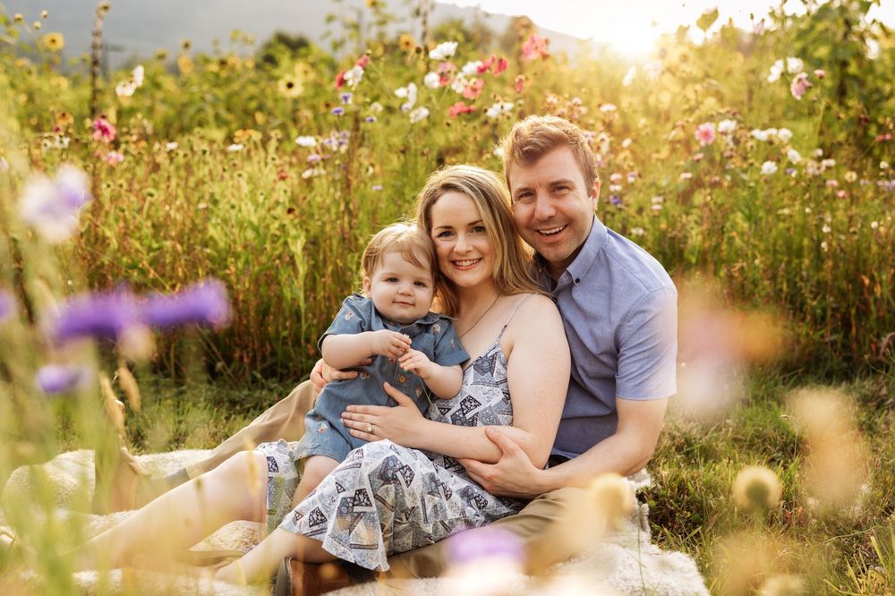 A happy family with a baby sits in a vibrant wildflower meadow during golden hour for a portrait session.