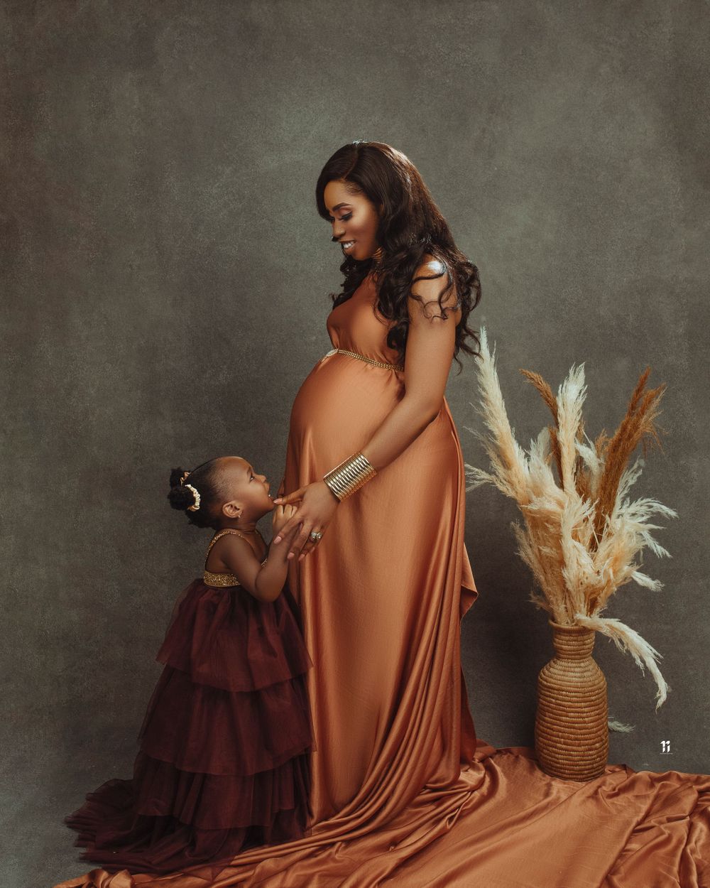 Artistic maternity photo with terracotta dress and dried pampas grass decor.