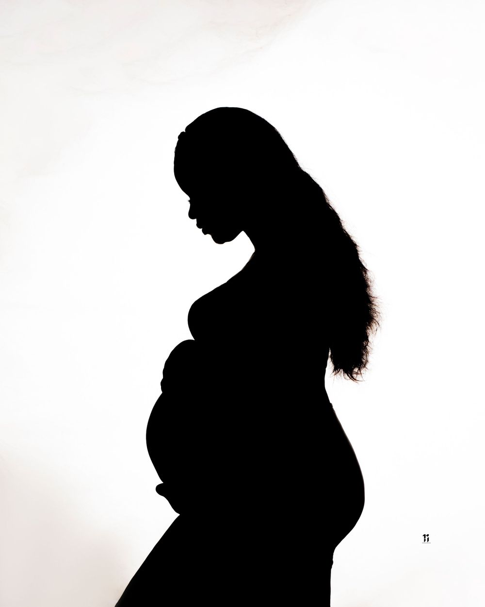 Dramatic silhouette of pregnant figure against white background highlighting baby bump.