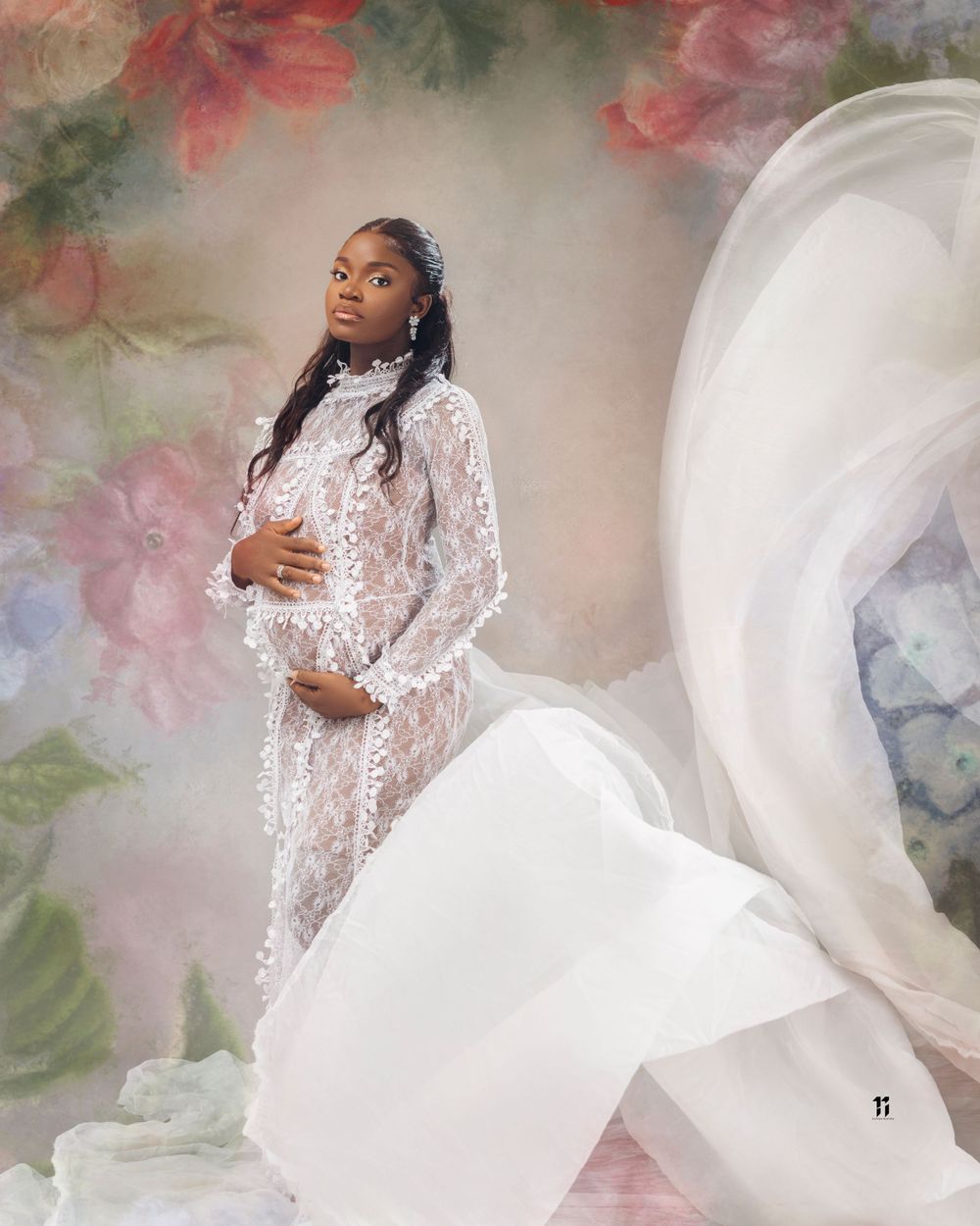 Ethereal maternity photo featuring flowing white lace gown against floral backdrop with soft pink roses.