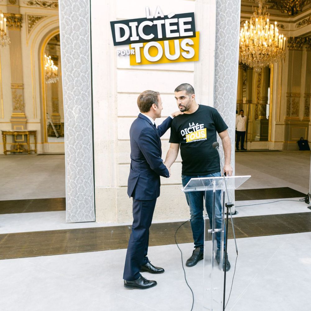 Discussion between two people at La Dictee Pour Tous event in an ornate room with chandeliers.