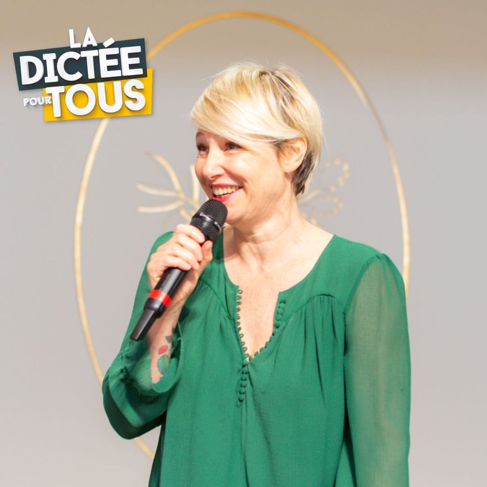 A person in a green blouse speaking into a microphone with a "La Dictee Pour Tous" logo in the background.