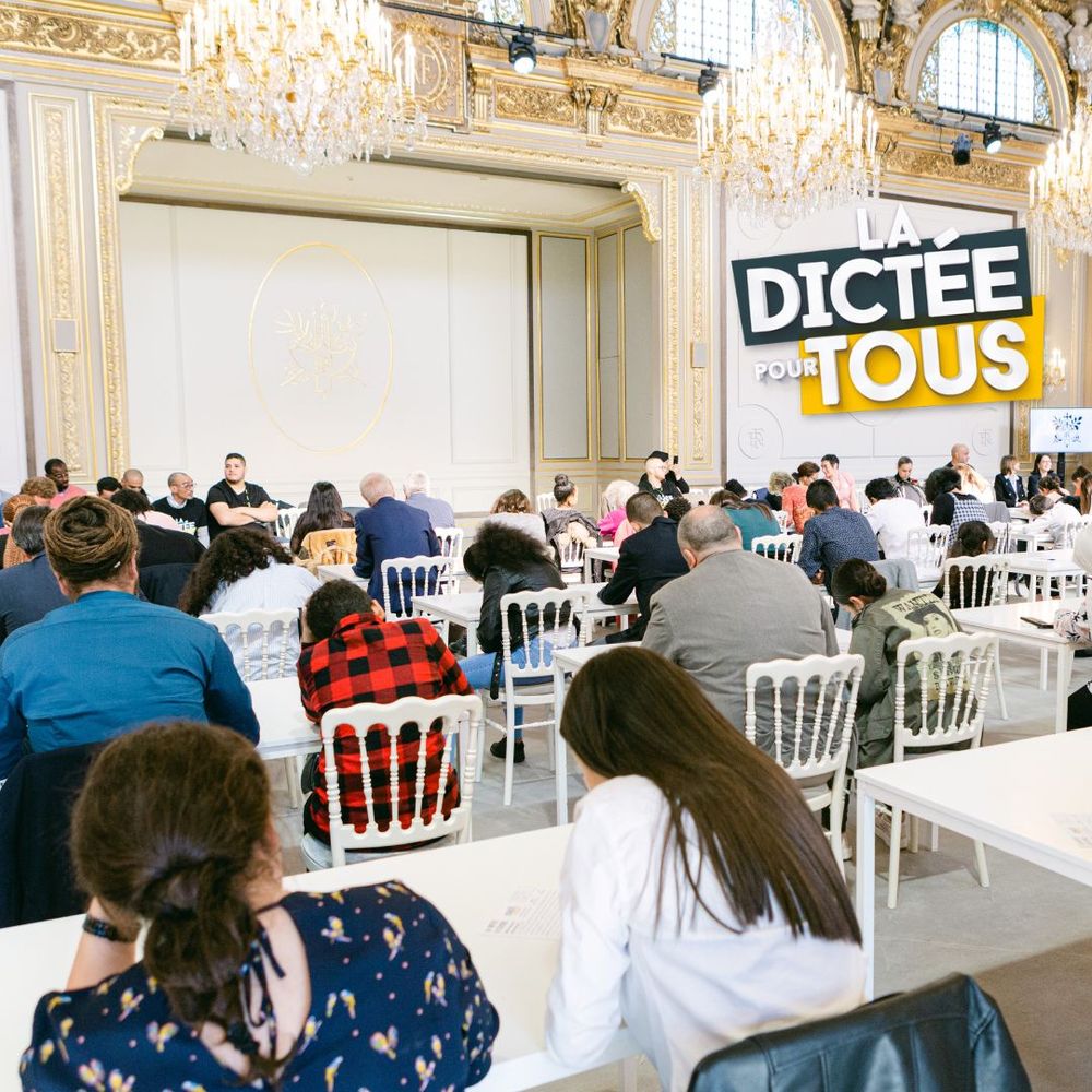 Audience seated in ornate ballroom with crystal chandeliers at business conference with Digitee Tous signage visible.