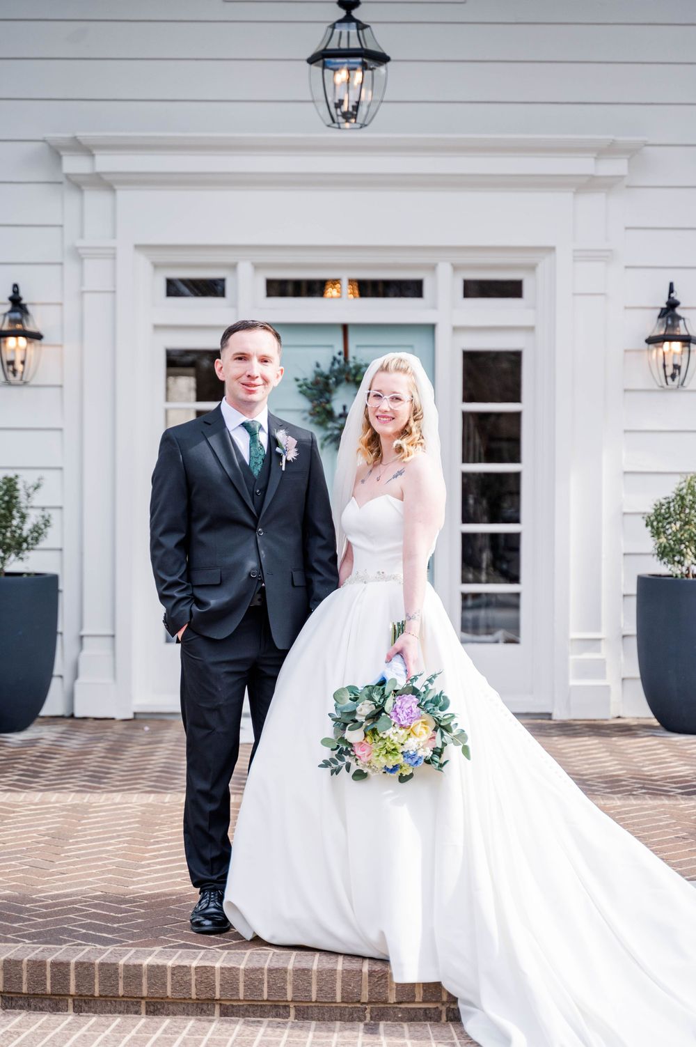 Classic wedding portrait on brick steps of white colonial house with lanterns.