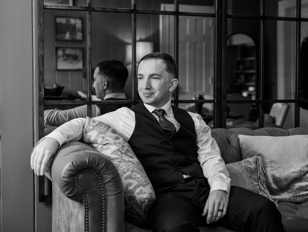 A black and white portrait of groom relaxing on an elegant vintage sofa. The Highgrove Estate, Fuquay-Varina, NC