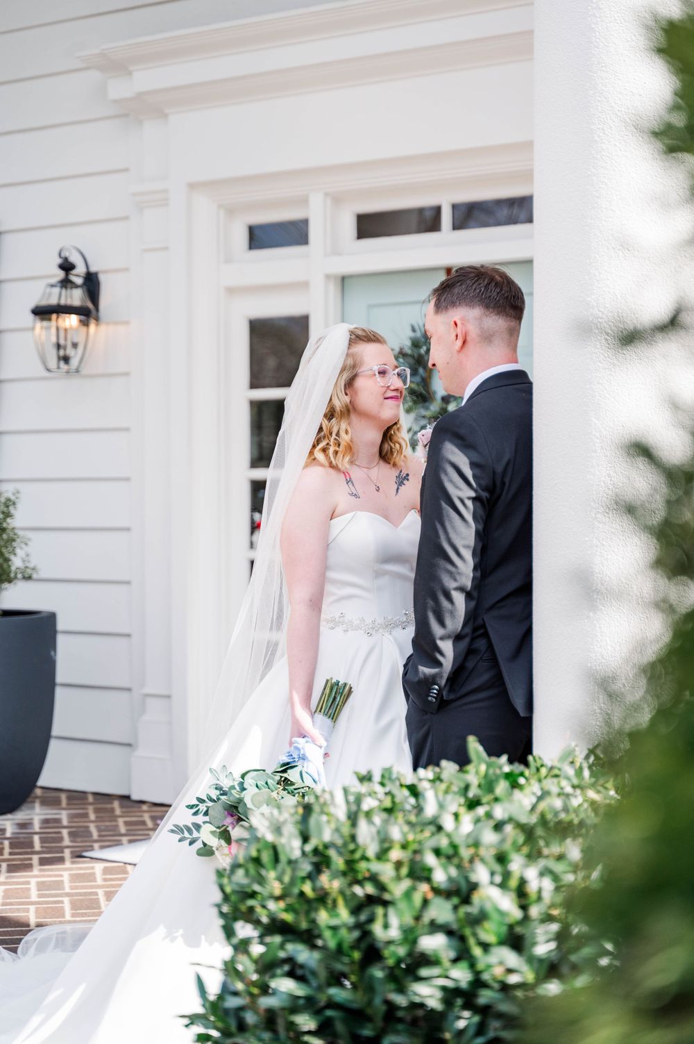 Candid wedding moment on white colonial porch with landscaping. The Highgrove Estate, Fuquay-Varina, NC