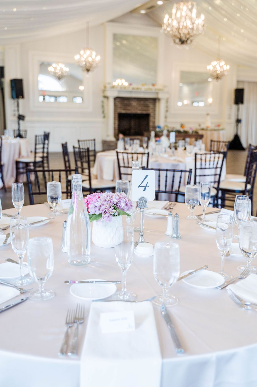 Elegant white reception venue with crystal chandeliers and round tables set for a celebration.