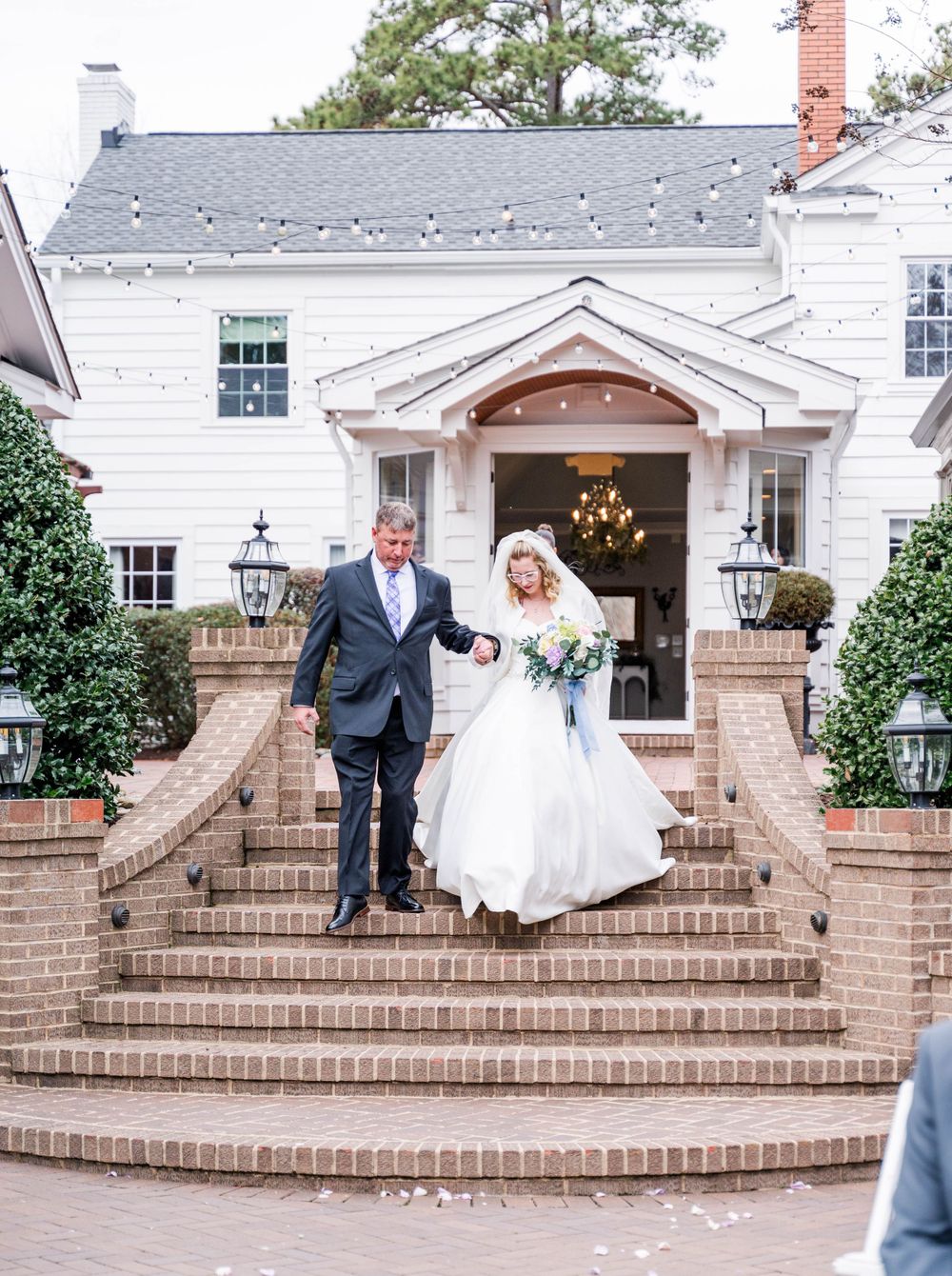Grand white house entrance with curved brick staircase decorated for wedding celebration.