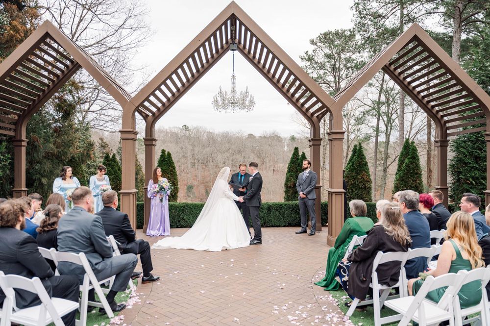 Outdoor wedding ceremony under wooden arch with chandelier and white chairs. The Highgrove Estate, Fuquay-Varina, NC
