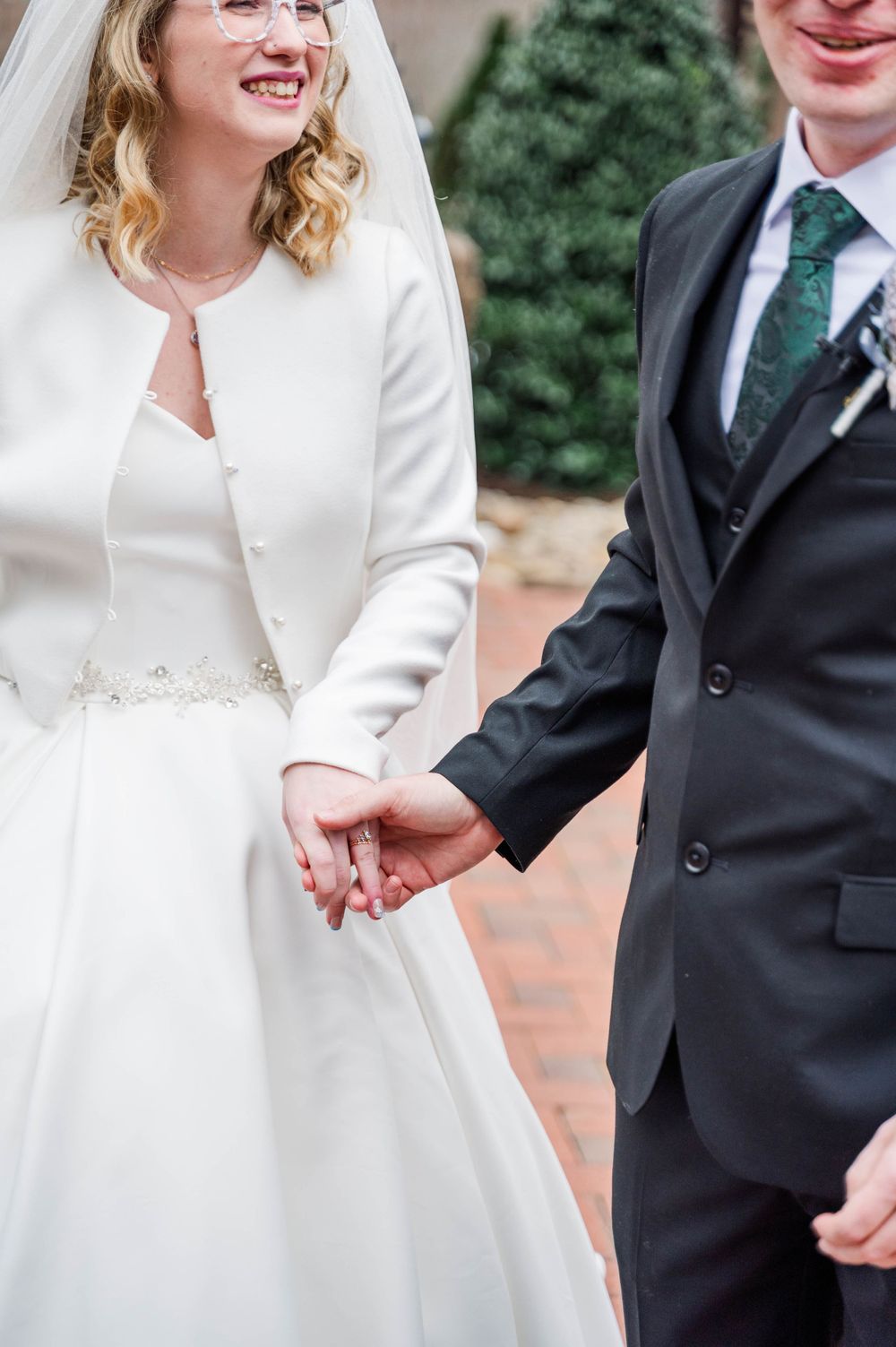 Close-up detail of couple holding hands, showing winter wedding attire with white dress and dark suit. The Highgrove Estate, Fuquay-Varina,