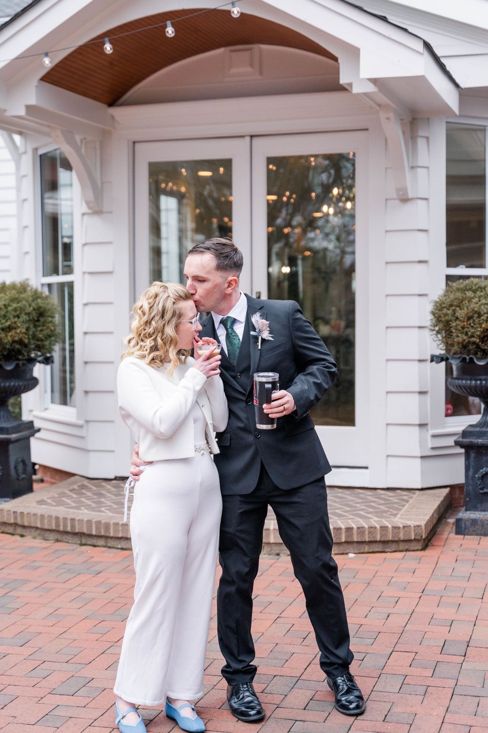 Couple shares intimate moment on brick patio outside elegant white venue. The Highgrove Estate, Fuquay-Varina, NC