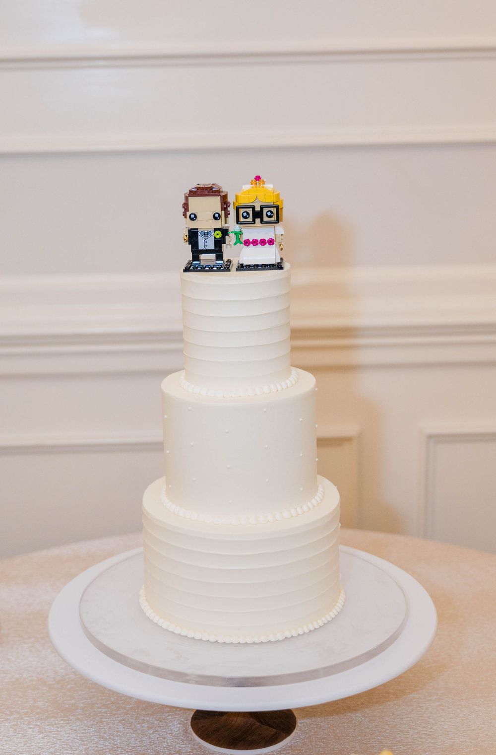 Three-tiered white wedding cake topped with pixelated 8-bit style cake topper.