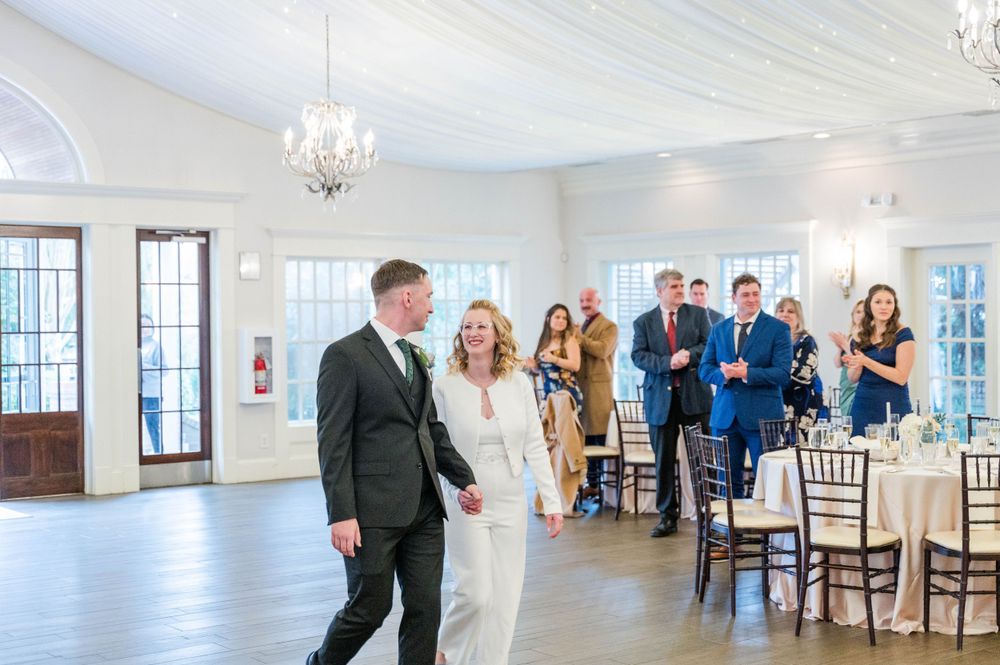 Wedding celebration in bright white reception hall with chandelier and hardwood floors.