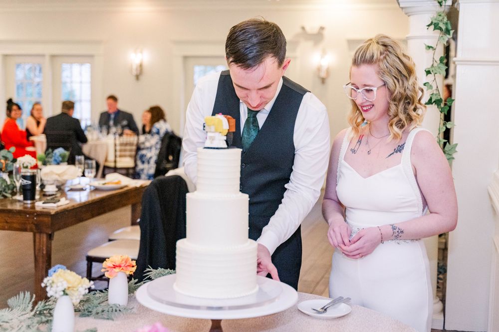 A couple shares a joyful moment while cutting their elegant white wedding cake.
