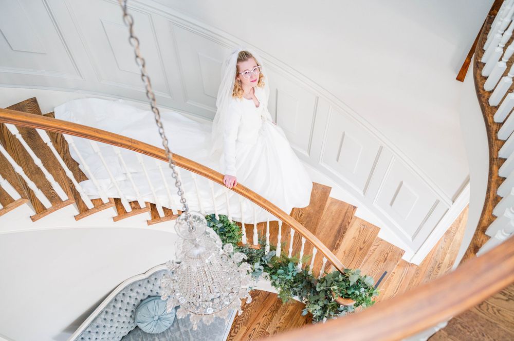 Bird's eye view of spiral staircase decorated with greenery and crystal chandelier. The Highgrove Estate, Fuquay-Varina, NC