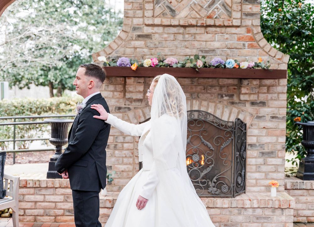 Romantic first look moment in front of a brick fireplace decorated with flowers.