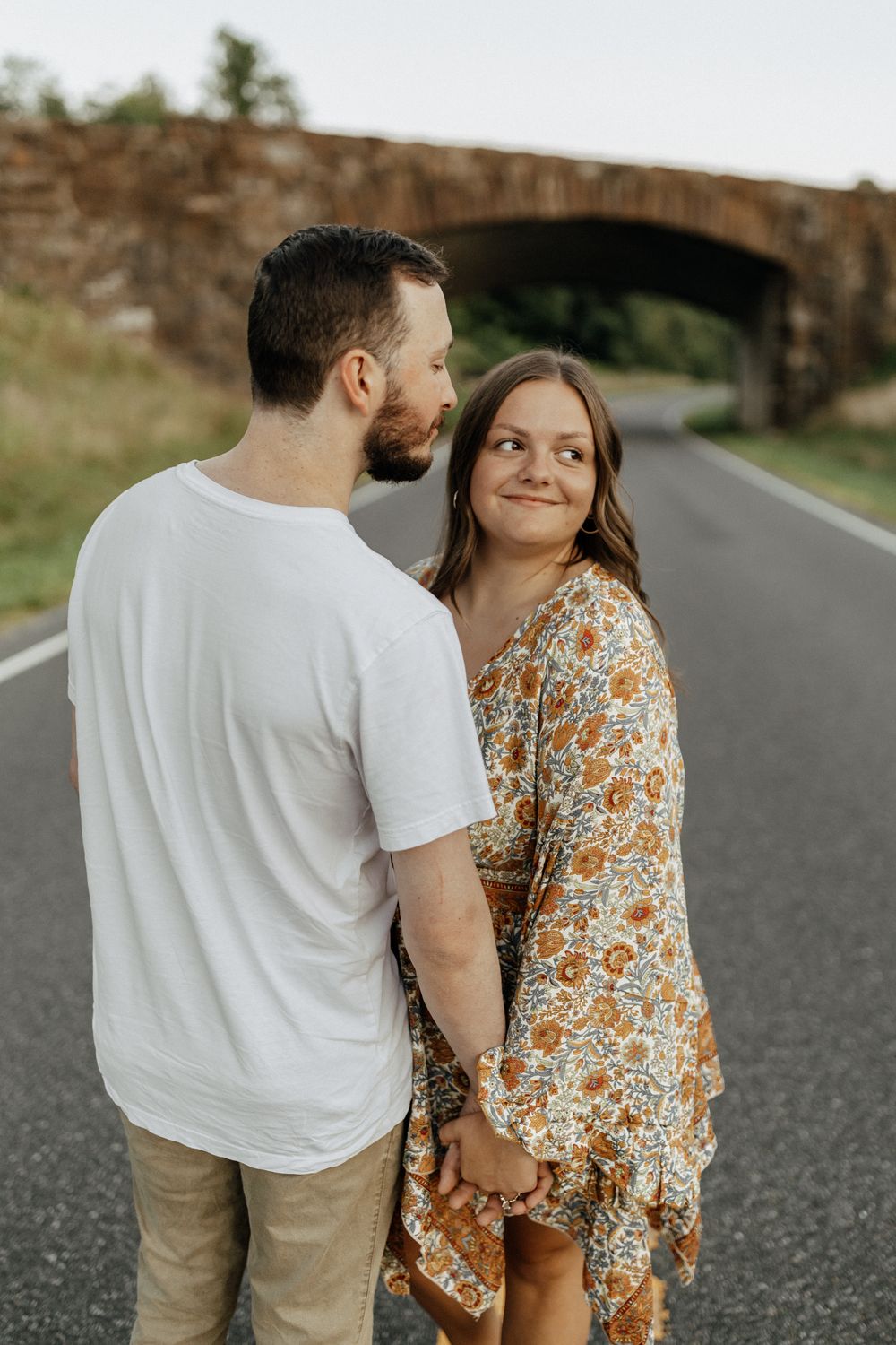 A couple sharing a romantic moment on a country road with stone bridge in background. Floyd, VA