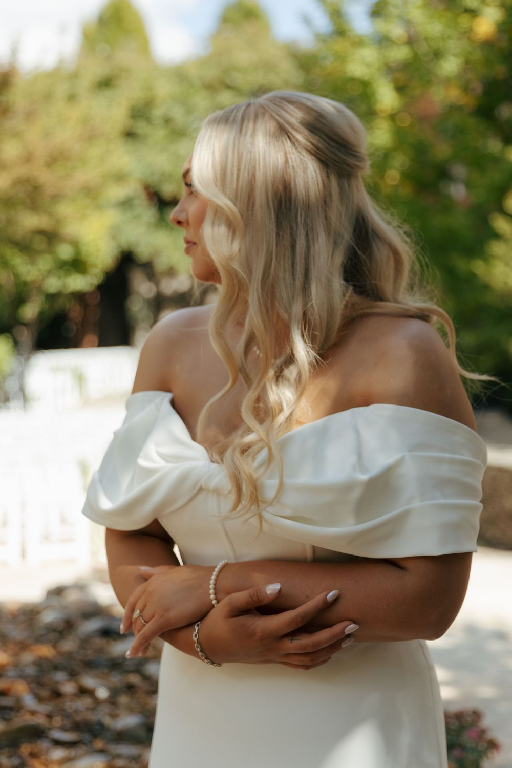 Bride in an elegant off-shoulder white dress poses in natural outdoor lighting.