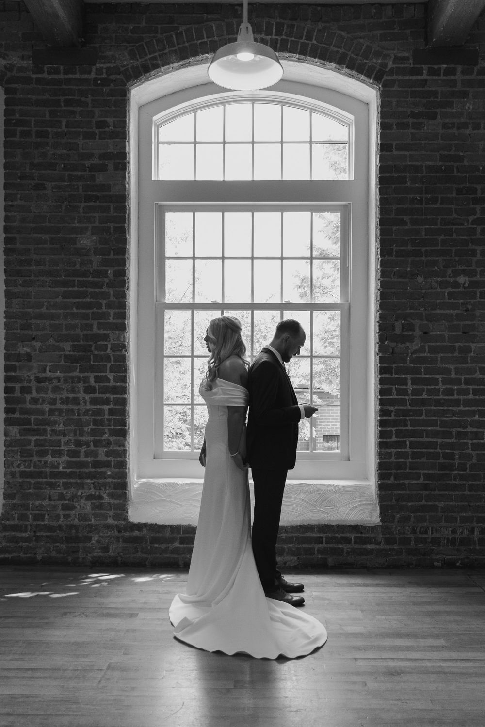 Silhouetted couple standing against a large arched window in a brick-walled venue.