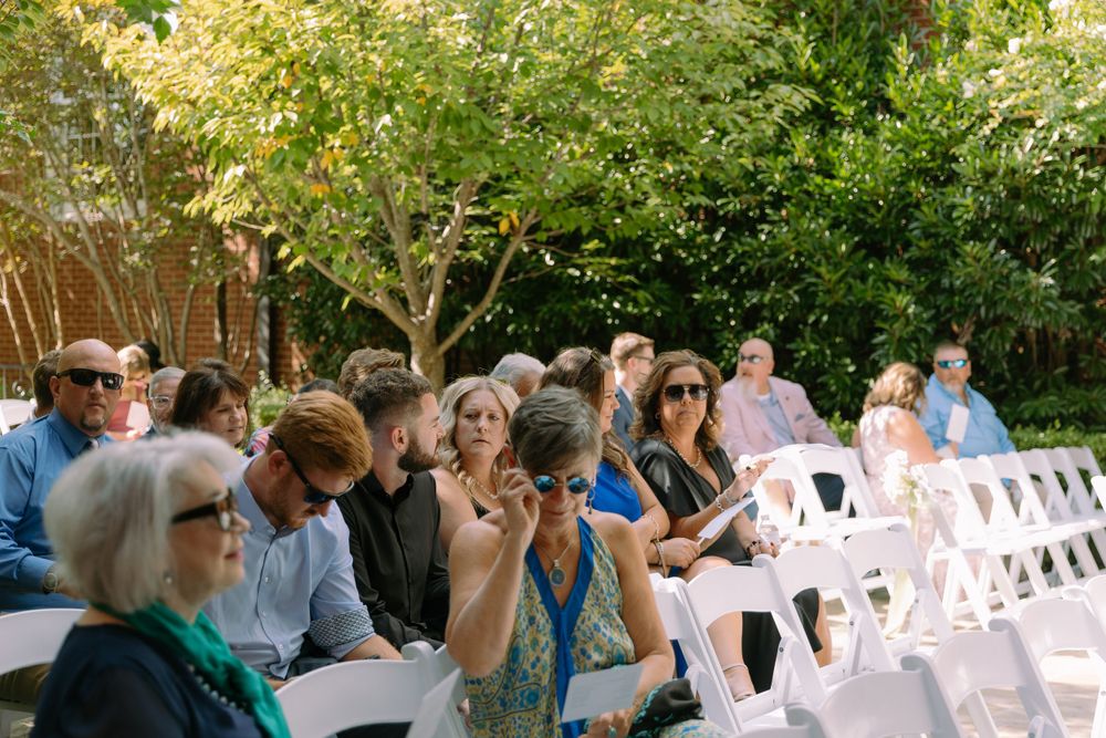 Wedding guests seated in white chairs outdoors during a daytime ceremony.