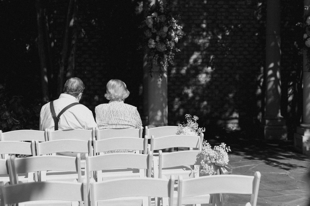 Black and white photo of guests seated in white chairs before an outdoor ceremony.