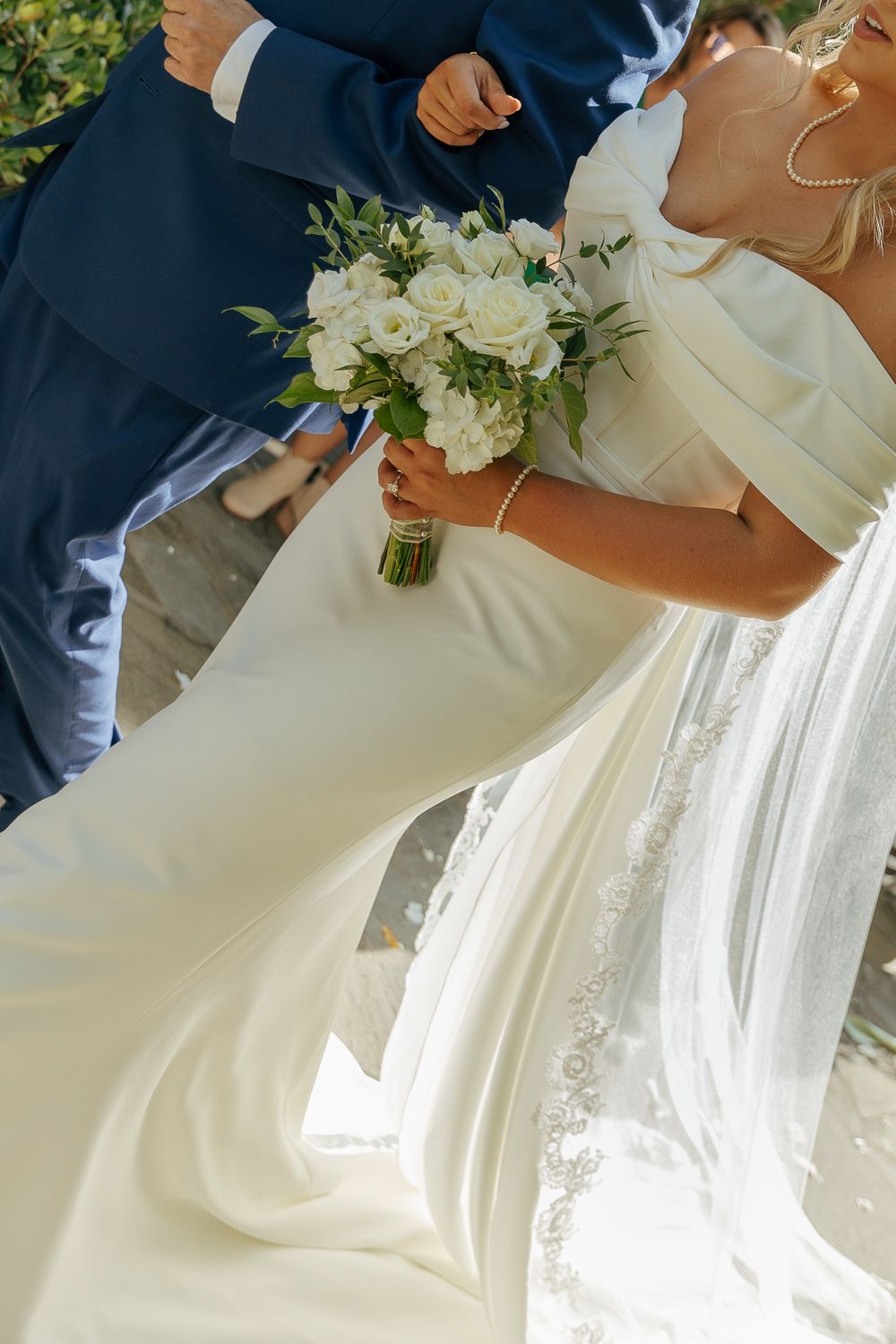 Close-up of bride holding white bouquet against flowing wedding dress.