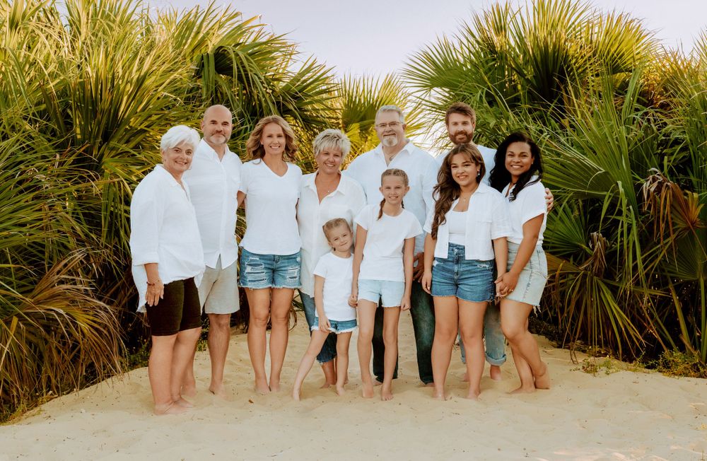 Family group portrait standing barefoot on a sandy path with tropical palm plants in the background on a sunny day.