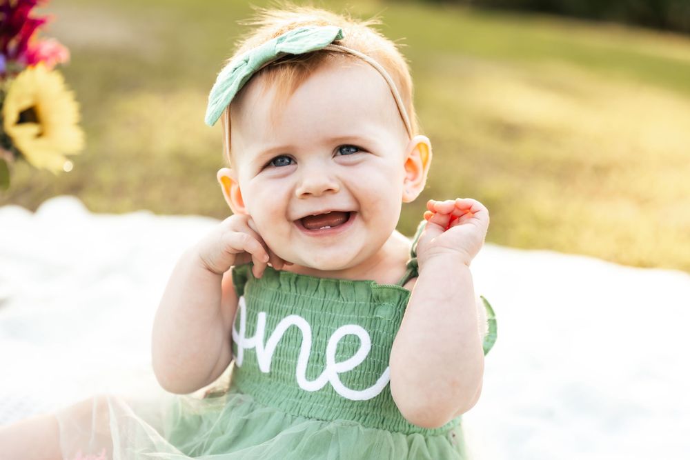 Baby wearing mint green outfit plays joyfully on grass during golden hour photoshoot.