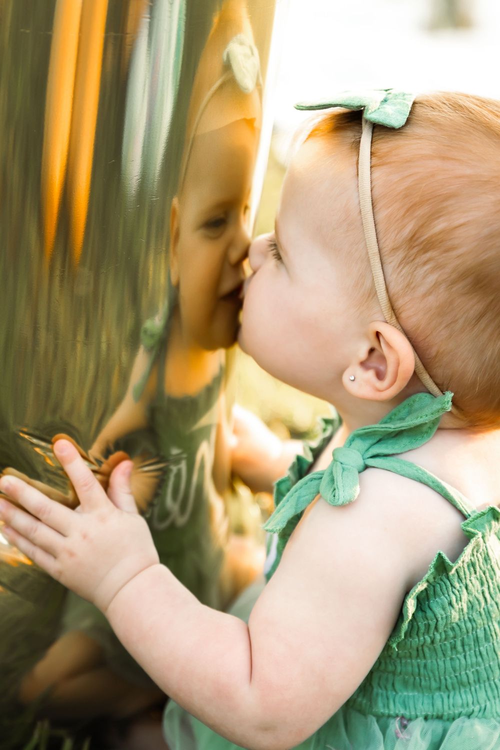 Baby in mint green dress and bow reaches up during indoor portrait session.