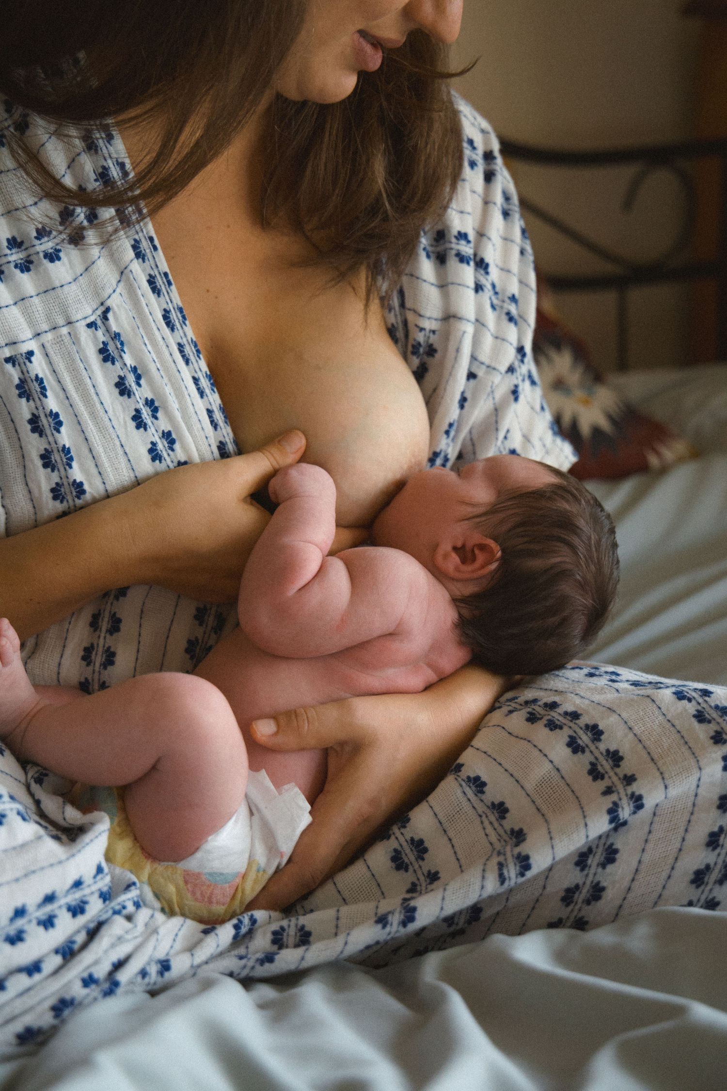 Mom nursing her newborn sitting on her bed during a newborn photoshoot in Vancouver, BC.