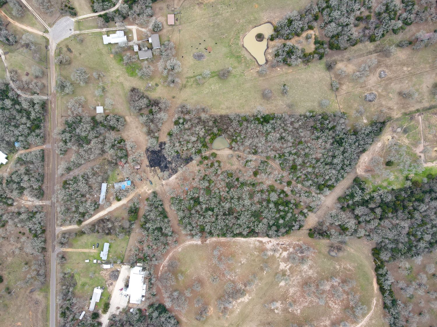 Aerial view of rural property with scattered buildings and wooded areas surrounded by dirt roads and clearings.