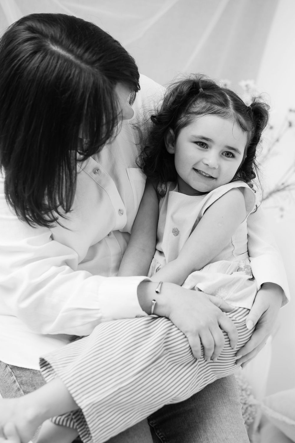 Black and white photo of tender moment between parent and young child sitting together in soft lighting.
