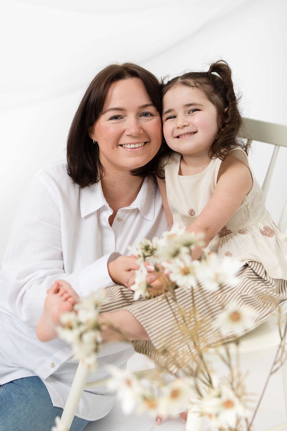 Sweet candid portrait with dried white flowers in foreground against light background.