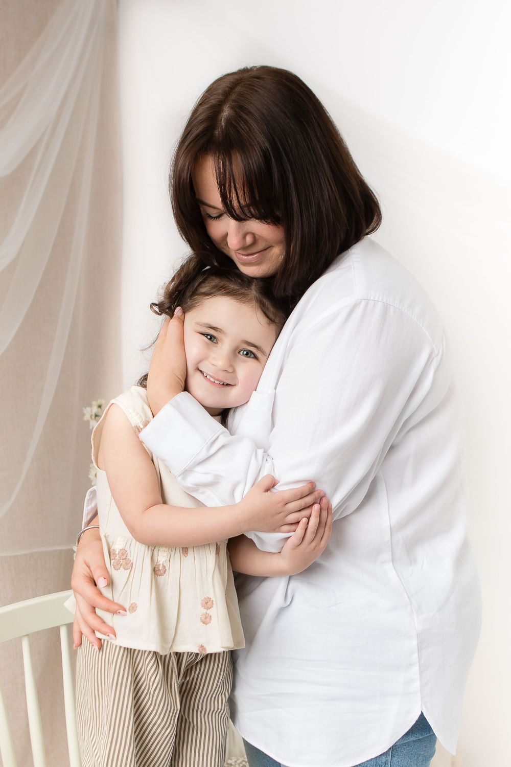 A loving embrace between parent and child wearing white clothing against a light background.