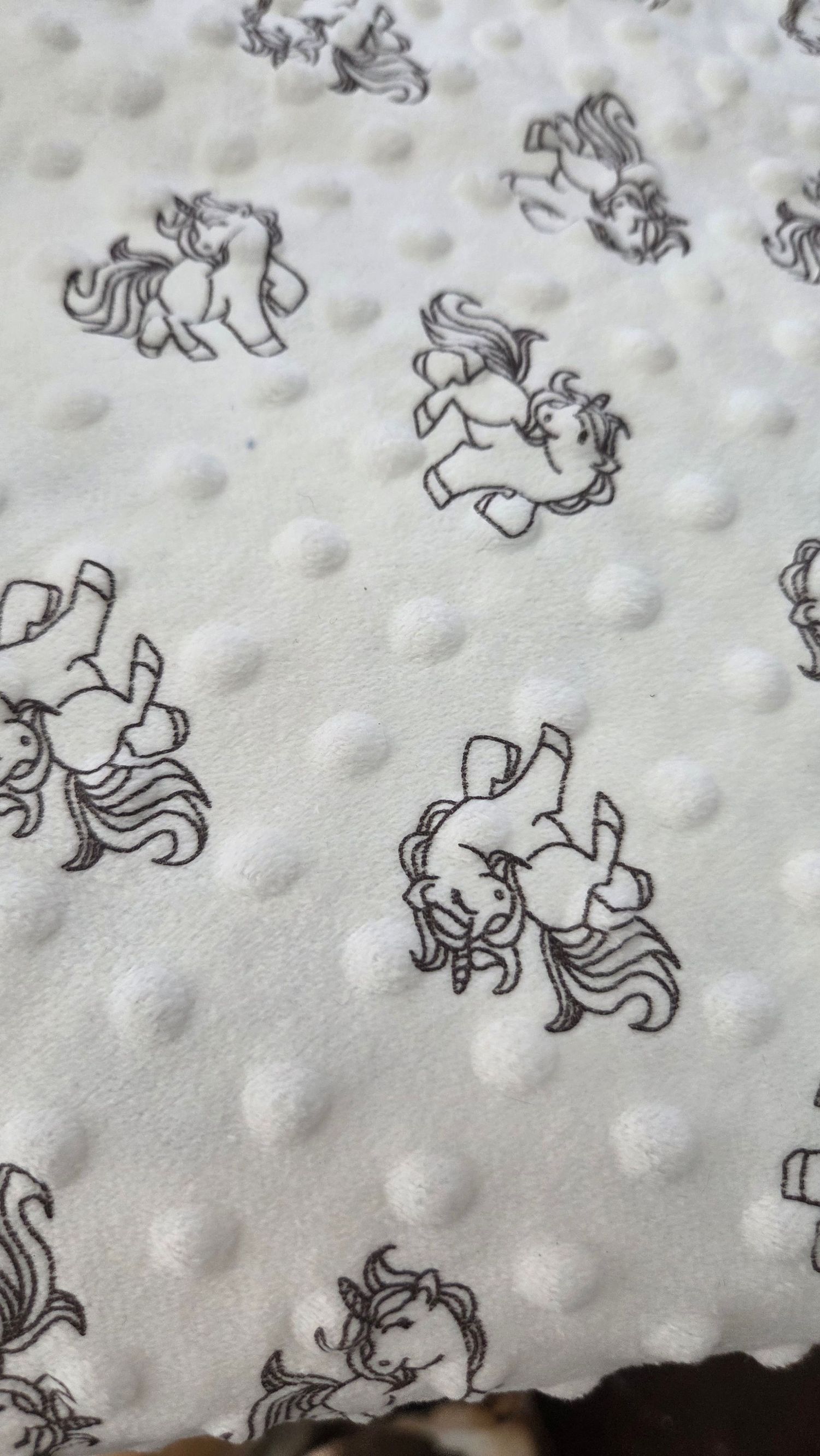 White minky dot fabric featuring black and white unicorn print pattern, soft textured baby blanket material.