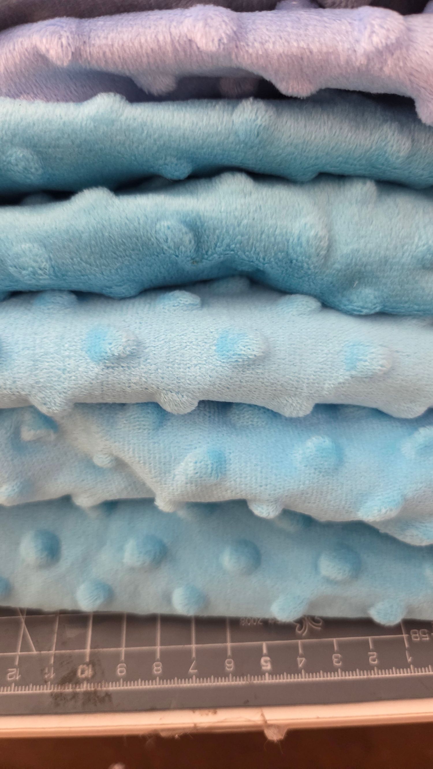 Stack of soft blue minky dot fabric in various shades, folded neatly on a cutting mat.