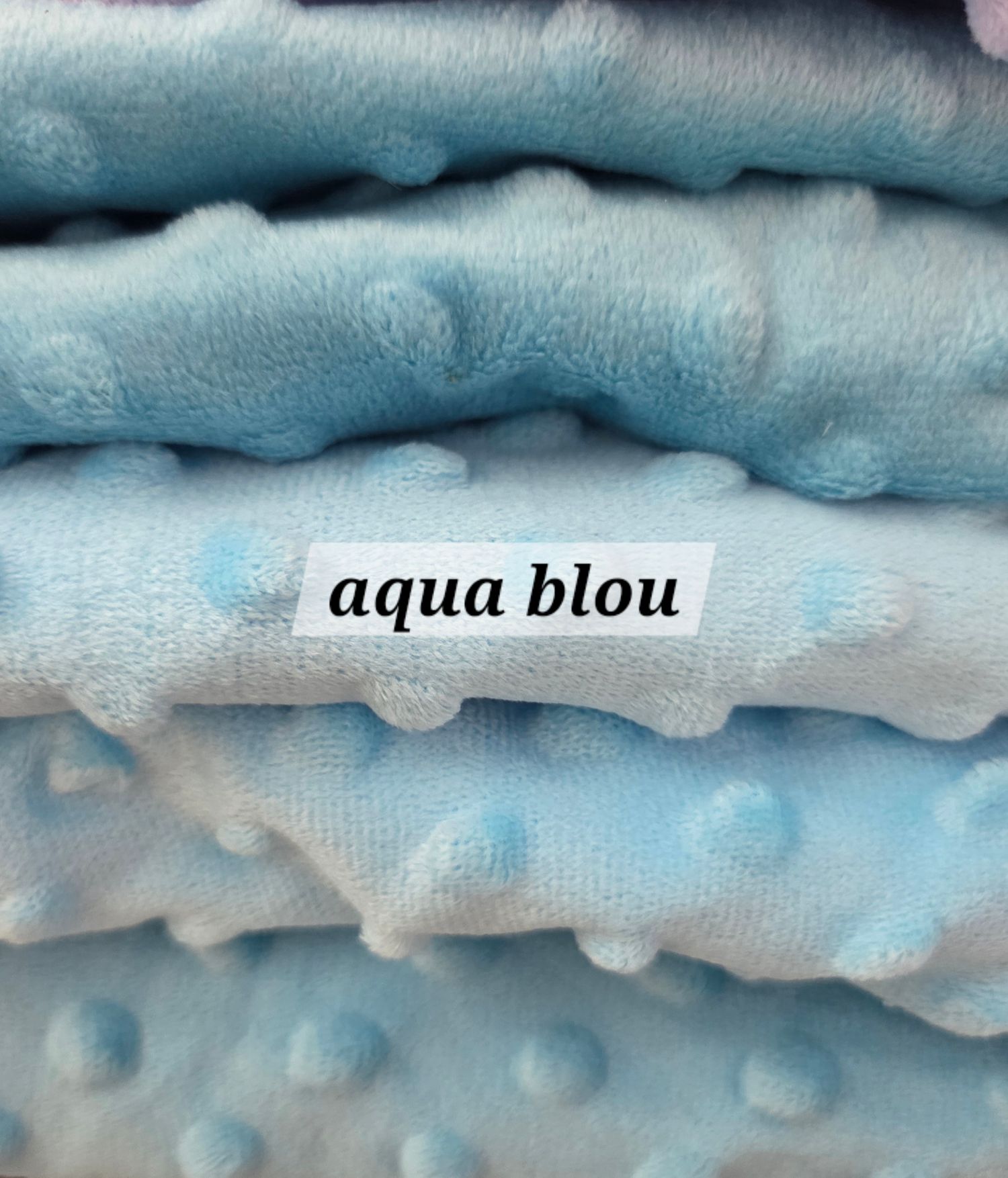 Soft aqua blue minky dot fabric with raised polka dot texture, labeled aqua blou, stacked in plush folds.