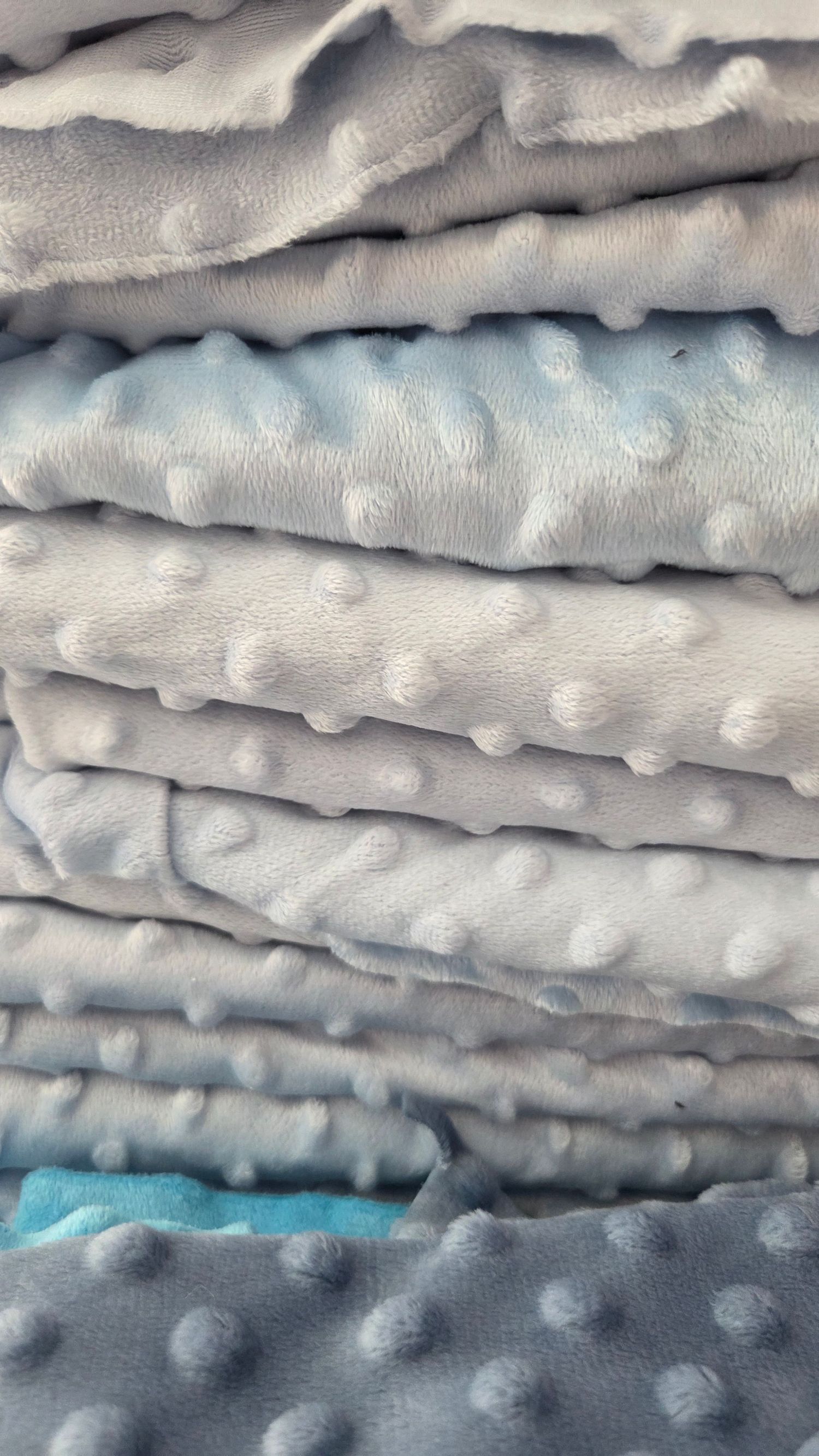 Stack of soft minky dot fabric in light blue and gray colors, folded neatly showing textured bubble pattern.