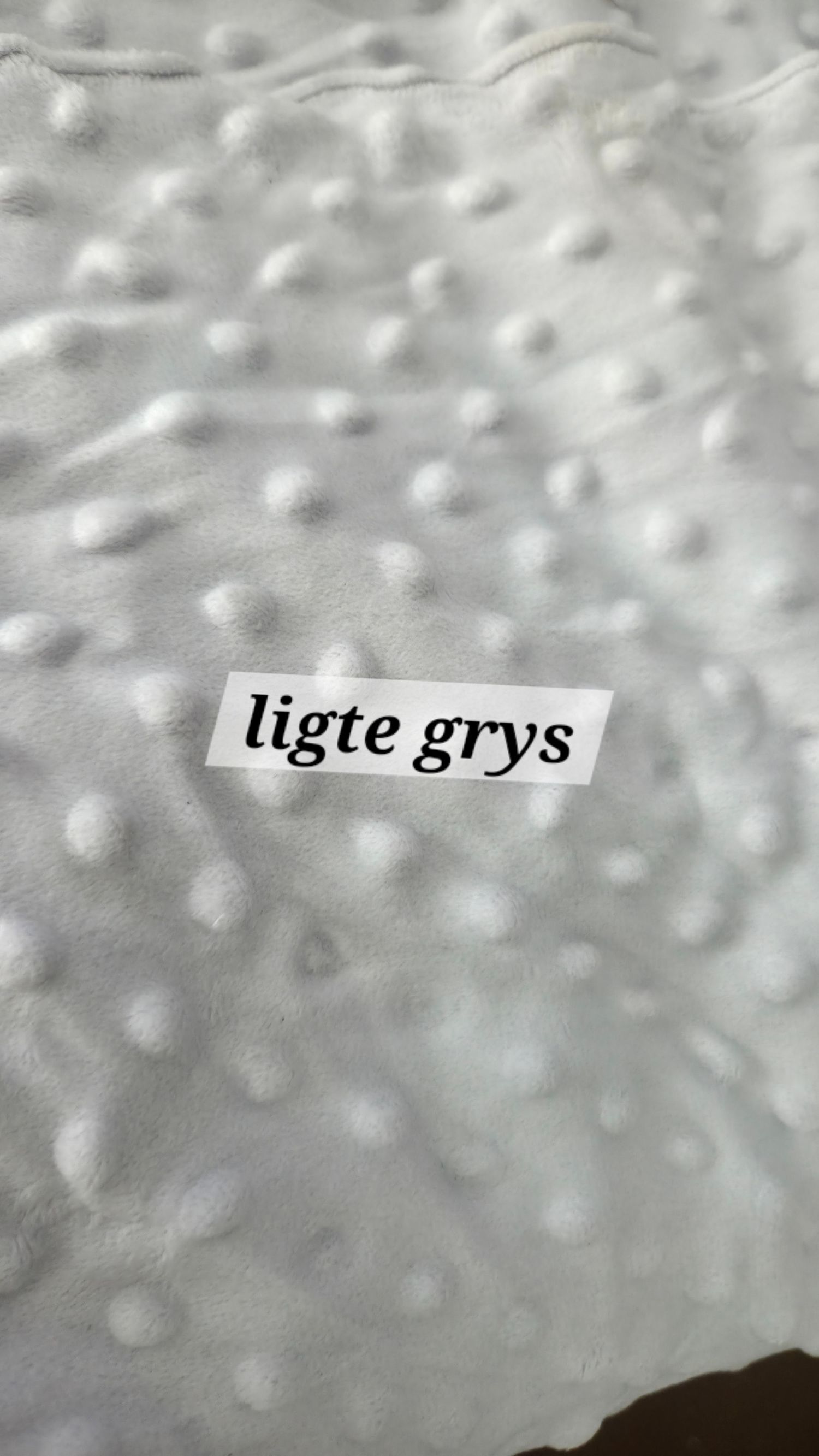 A white textured fabric with raised dot pattern and a label reading 'ligte grys' meaning light grey.