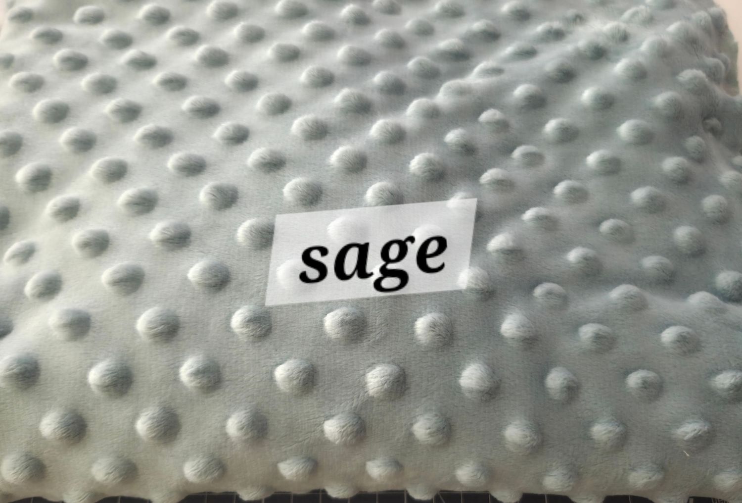Close-up of sage green minky dot fabric swatch with raised polka dot texture, labeled with color name sage.