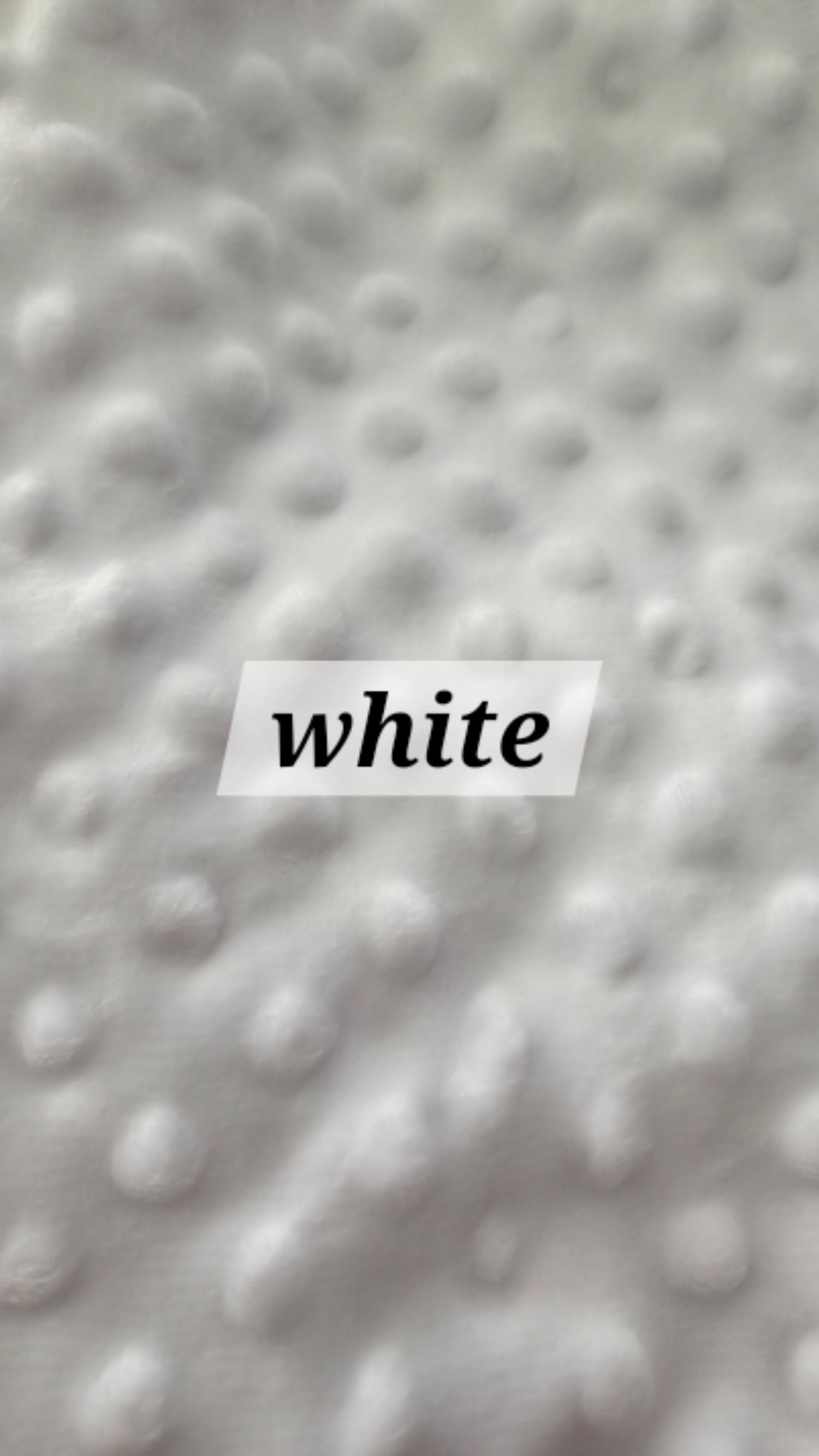 Close-up of white minky dot fabric with raised polka dot texture, labeled white.