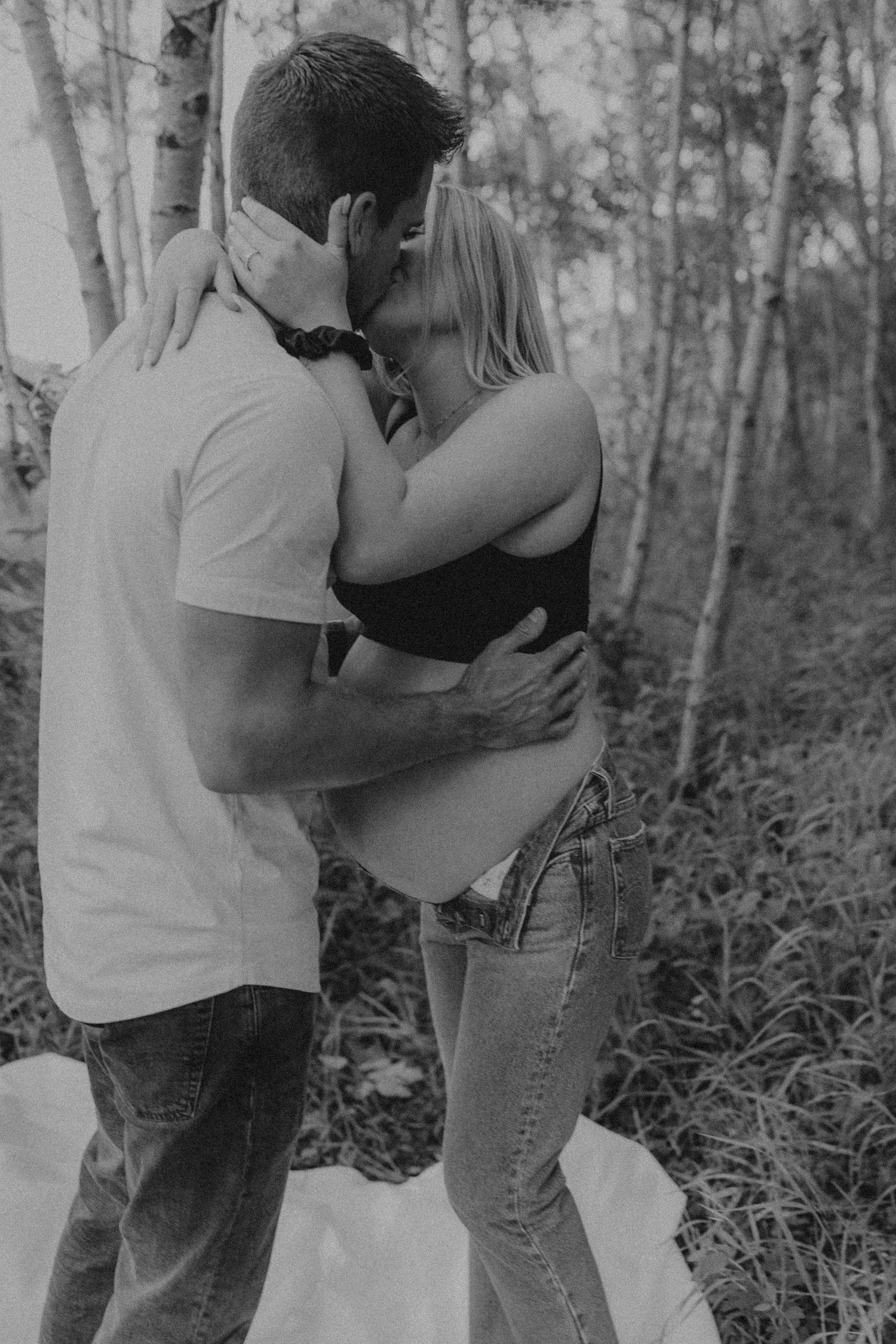Romantic black and white photo of a couple embracing in a forest of birch trees.