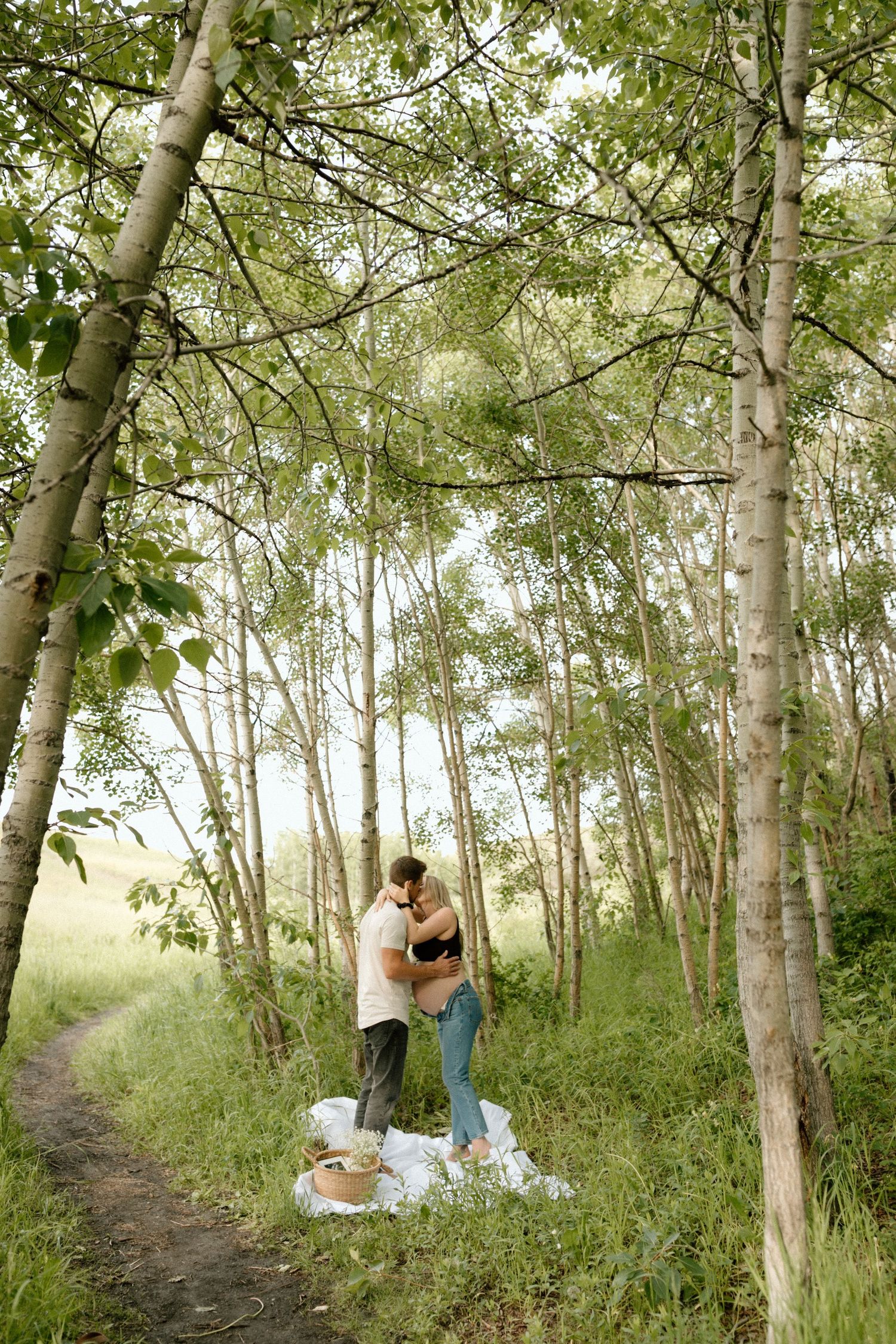 An intimate moment captured between a couple on a white blanket surrounded by birch trees.