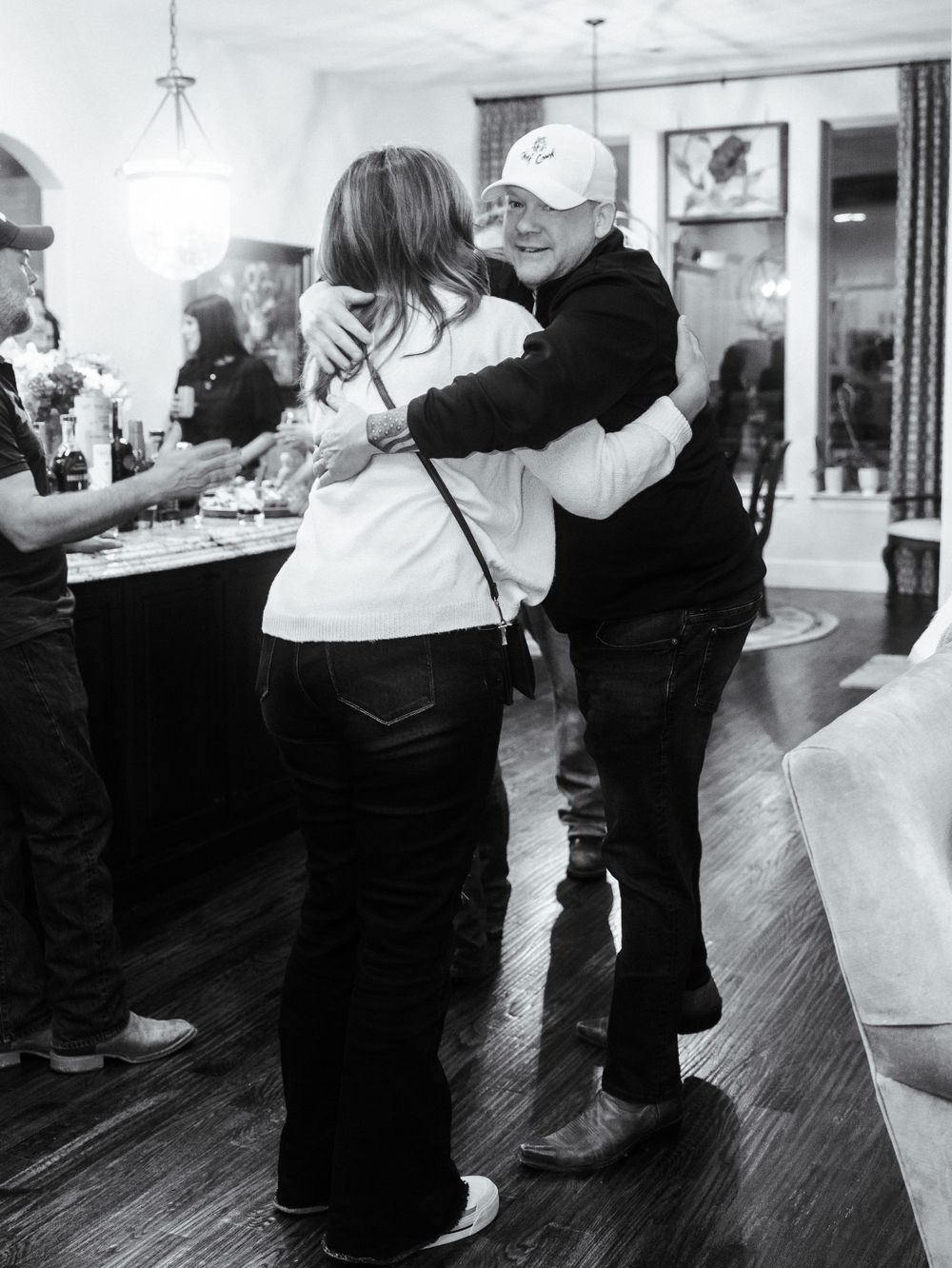 Black and white photo of people embracing at an indoor gathering.