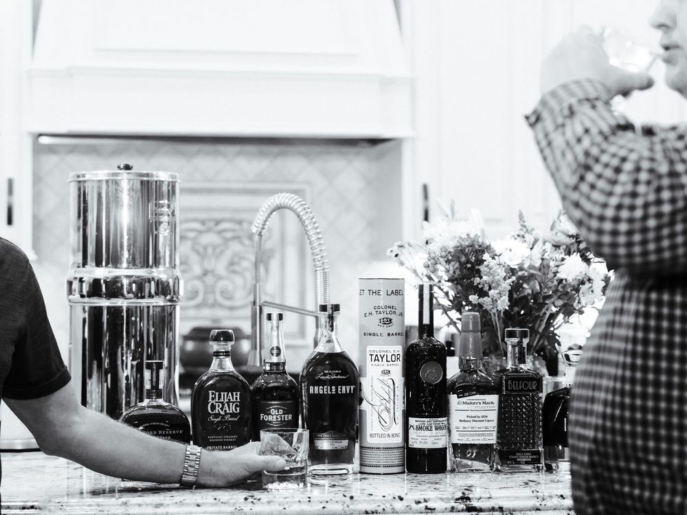 A black and white photo of various liquor bottles and cocktail ingredients arranged on a bar counter.