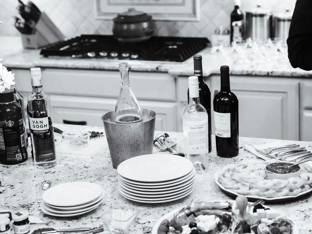 Party setup with wine bottles, stacked plates and glassware on a kitchen counter.